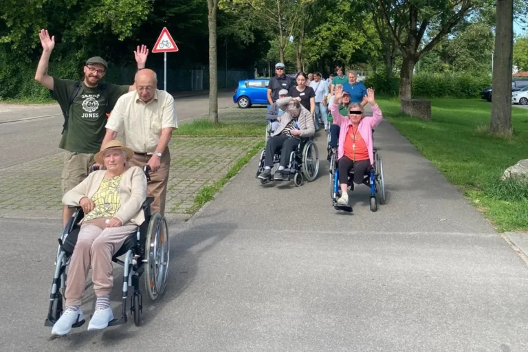 Bewohnerinnen und Bewohner kehren im Rollstuhl begleitet von Helfern singend ins Seniorenzentrum zurück.