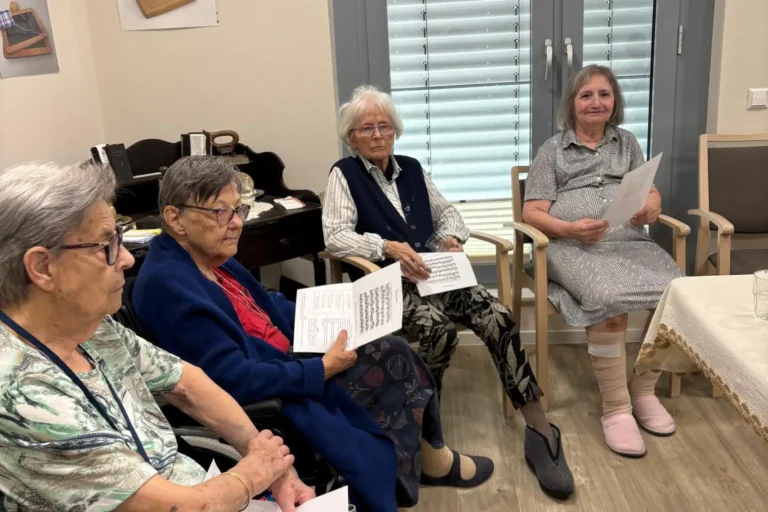 Vier Bewohnerinnen sitzen nebeneinander mit Notenblättern und hören konzentriert der Musik zu.