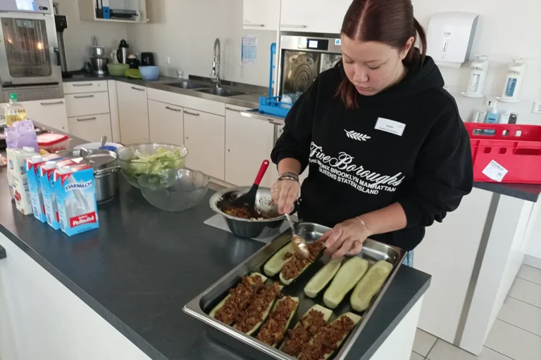Eine junge Frau füllt die vorbereiteten Zucchinihälften mit Hackfleischmasse in einer großen Küche.