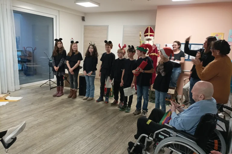 Der Heilige Nikolaus steht neben den Schülerinnen und Schülern während der Nikolausfeier im Pflegeheim.