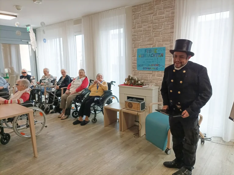 Schornsteinfeger im schwarzen Zylinder steht neben einer Mitarbeiterin mit Mikrofon im Seniorenzentrum.