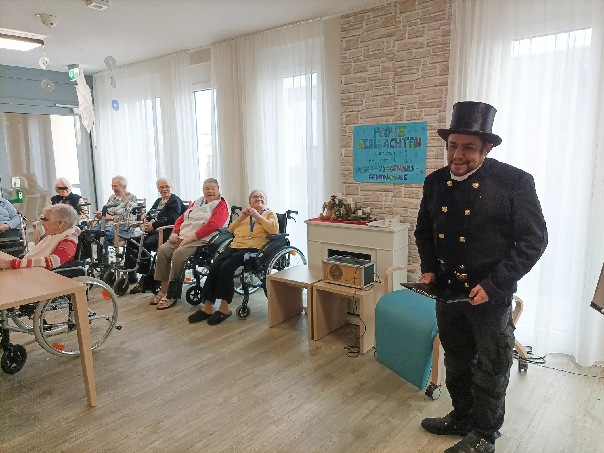 Schornsteinfeger im schwarzen Zylinder steht neben einer Mitarbeiterin mit Mikrofon im Seniorenzentrum.