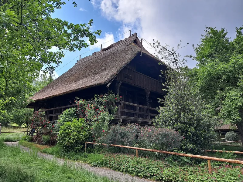 Reetgedecktes Bauernhaus mit Blumen und Bäumen im Vordergrund, Teil des Freilichtmuseums Vogtsbauernhof.