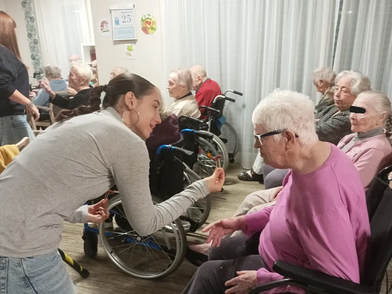 Eine junge Frau spricht lächelnd mit einer Seniorin im Rollstuhl während der Theateraufführung.