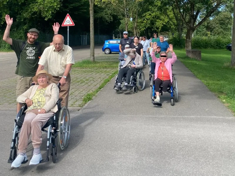Bewohnerinnen und Bewohner kehren im Rollstuhl begleitet von Helfern singend ins Seniorenzentrum zurück.