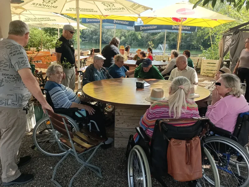 Bewohnerinnen und Bewohner sitzen unter Sonnenschirmen direkt am Wasser bei Kaffee und Eis.