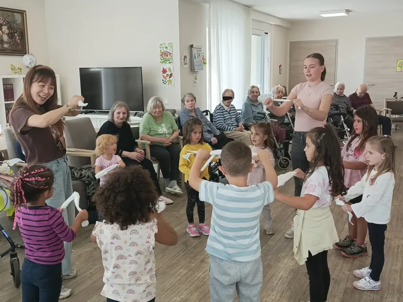 Kinder der Kita Sundheim singen fröhlich im Stehen, während Seniorinnen aufmerksam zusehen.