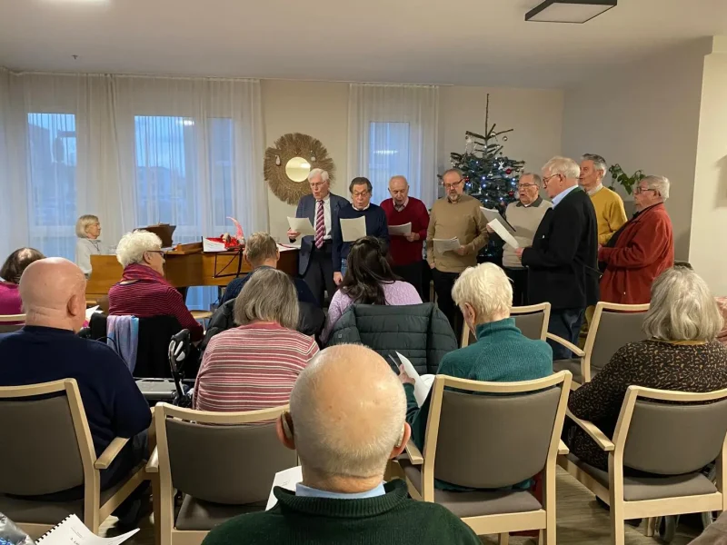 Eine Gruppe Männer singt gemeinsam Weihnachtslieder vor den Bewohnern des Seniorenzentrums, begleitet vom Klavier.