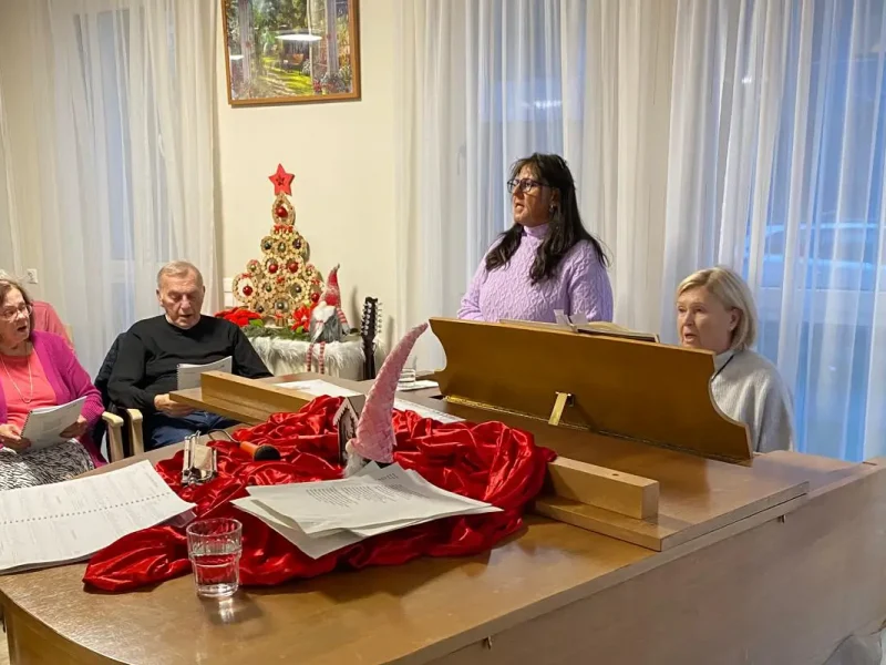 Bewohnerinnen und Bewohner des Seniorenzentrums singen gemeinsam Weihnachtslieder, begleitet von Klaviermusik in festlich geschmückter Atmosphäre.