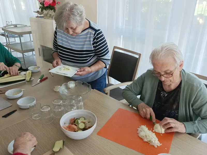 Bewohnerinnen schneiden Zwiebeln und Zucchini und bereiten die Zutaten für das Kochprojekt vor.