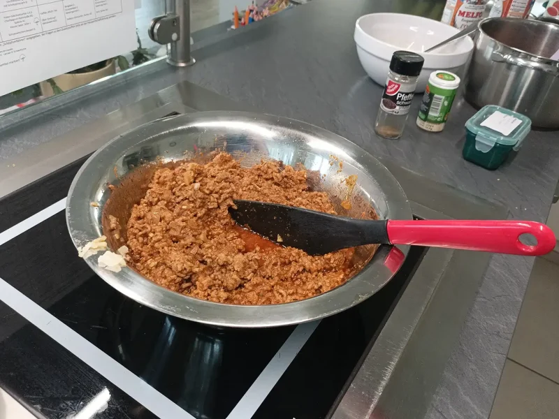 Eine Pfanne mit angebratenem Hackfleisch und Tomatenmark steht auf dem Herd.