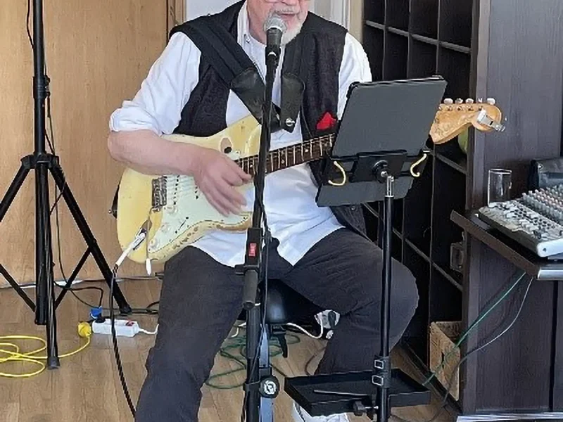 Musiker mit E-Gitarre und Mikrofon bei einem Live-Auftritt in einer Senioreneinrichtung.