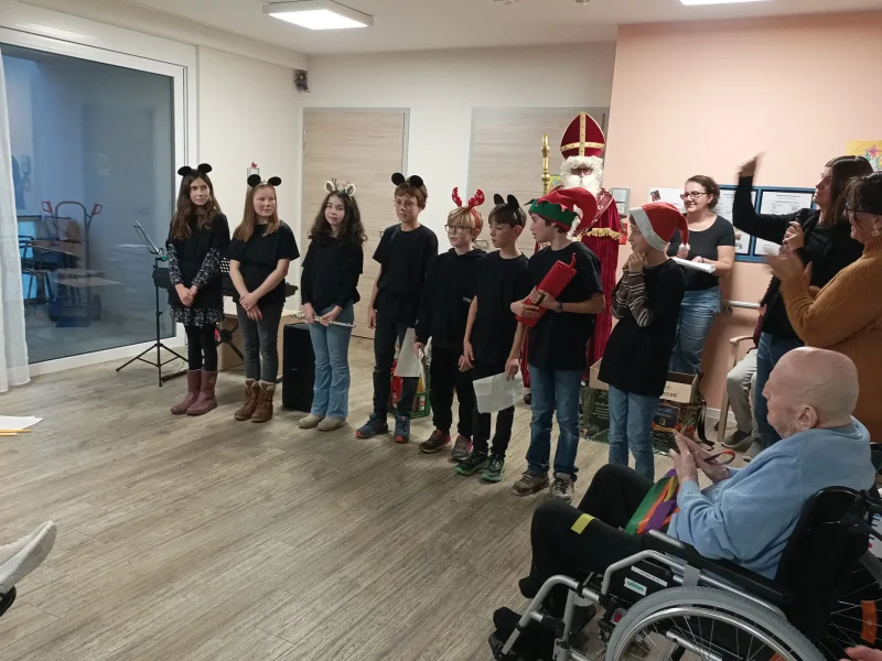 Der Heilige Nikolaus steht neben den Schülerinnen und Schülern während der Nikolausfeier im Pflegeheim.